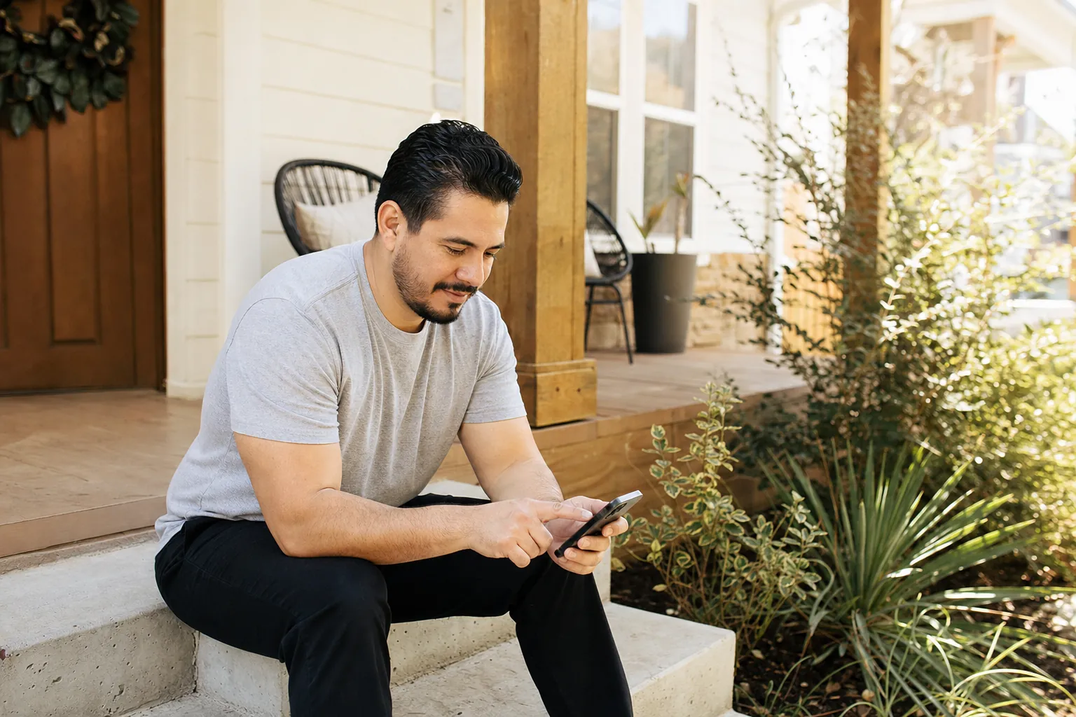 A man on his front porch steps tapping his phone