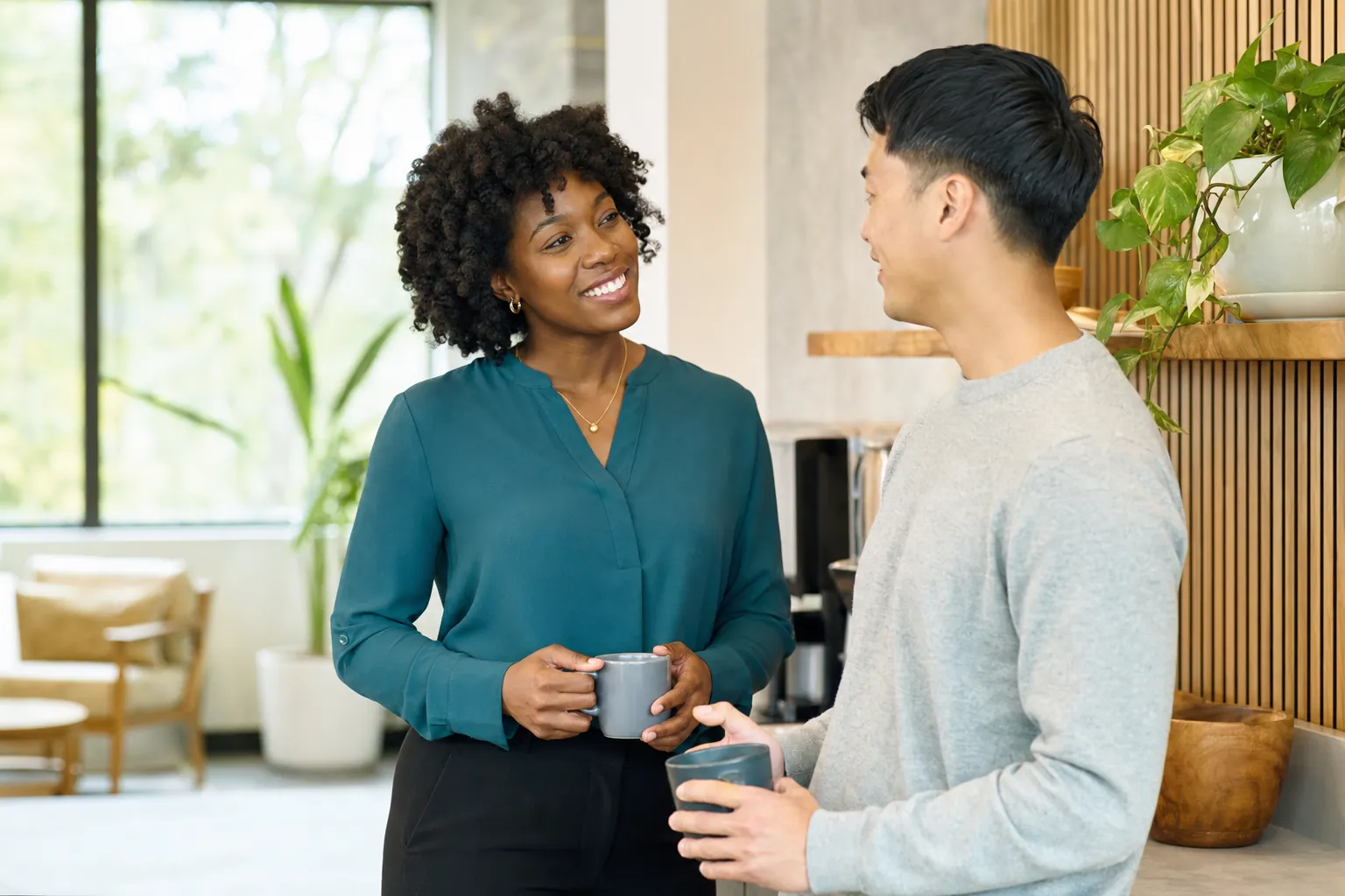 Two colleagues chatting over coffee in a bright office kitchen