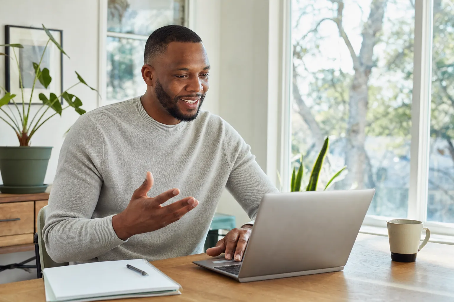 A man on a video call at a home desk with a notepad