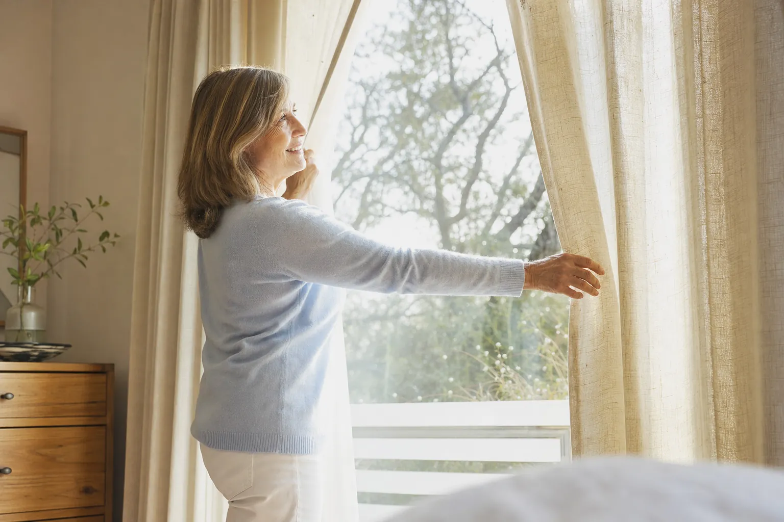 A woman opening curtains to morning sunlight