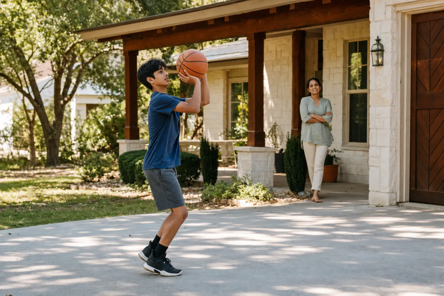 A teenage boy shooting hoops in a sunny driveway