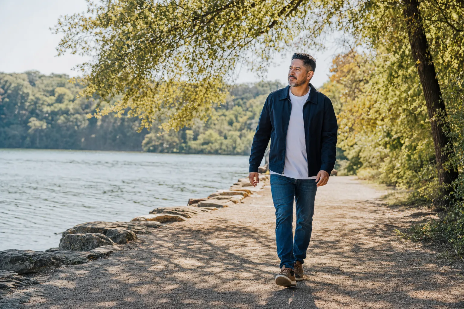 A man walking alone on a sunny lakeside trail