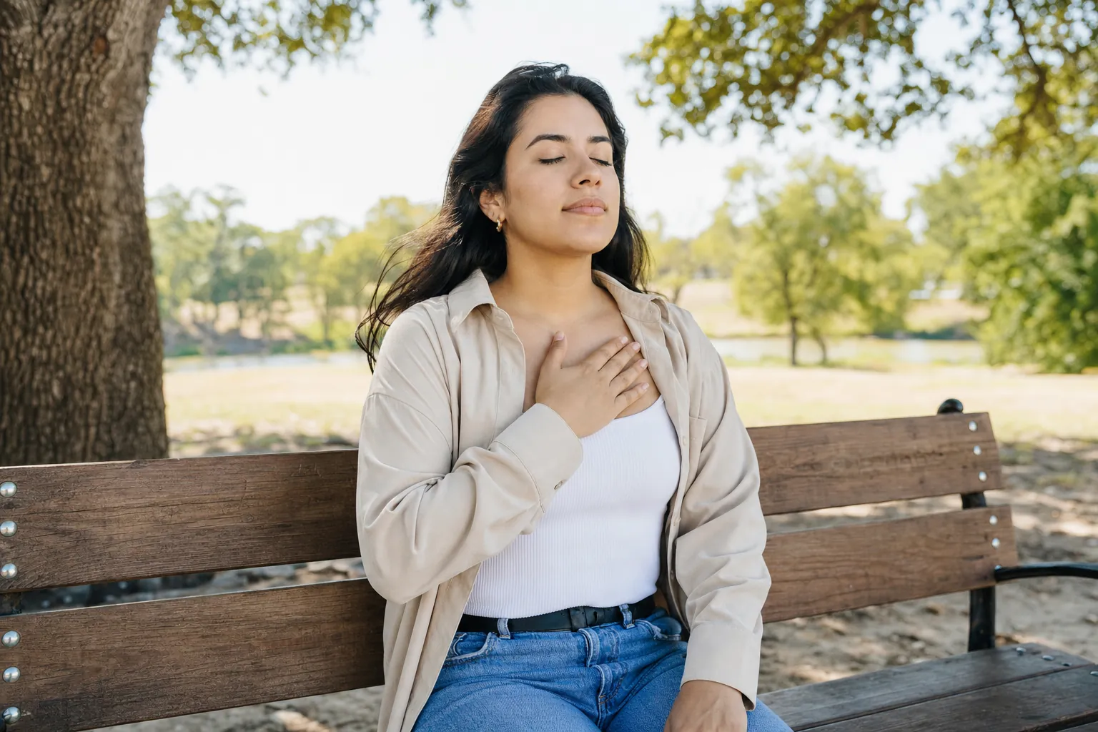 A young woman on a park bench breathing slowly with a hand on her chest