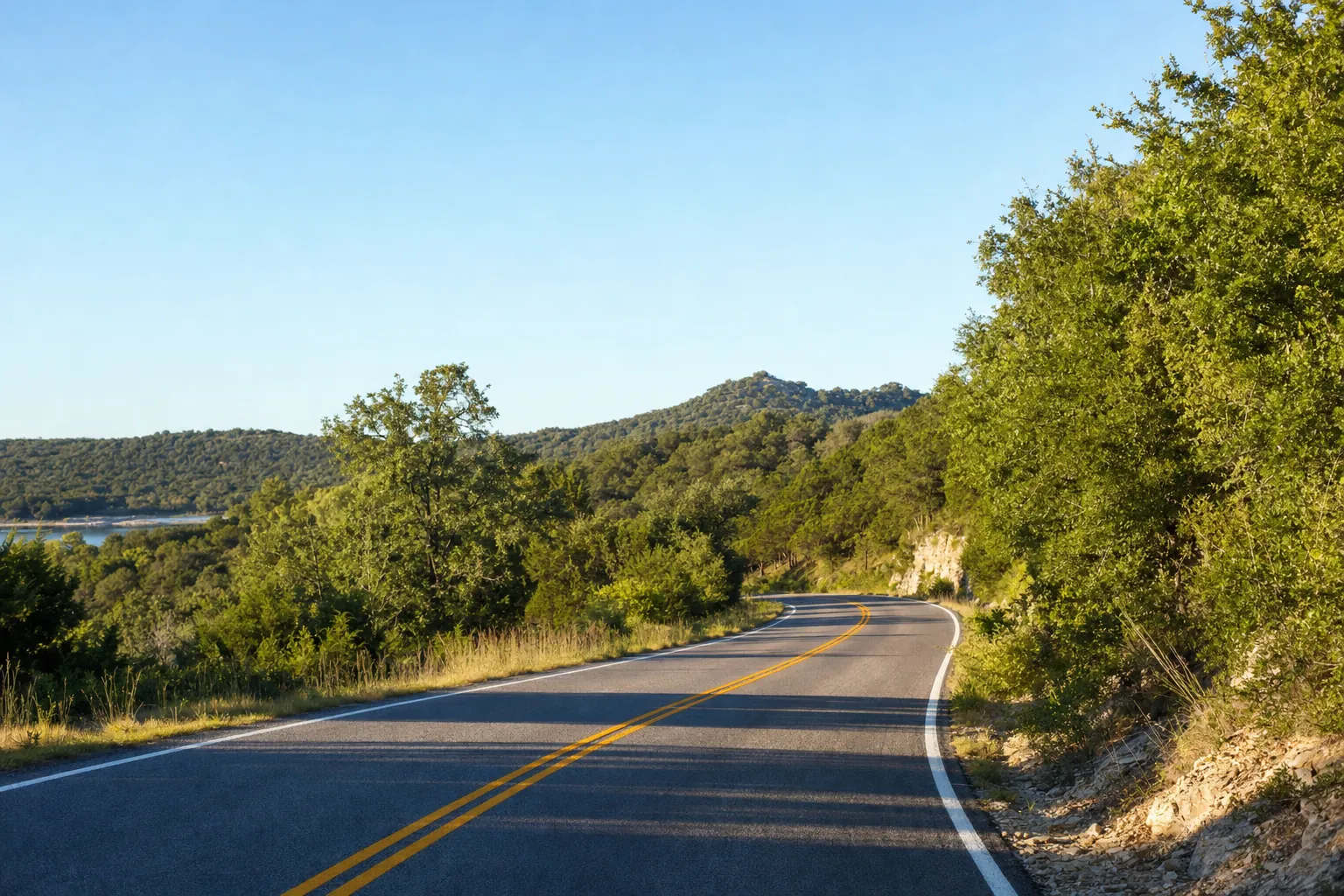 A road winding through green Texas hills under a blue sky